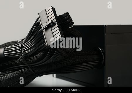 black 24-pin atx motherboard connector and bundled mesh-sleeved cables from pc power supply unit isolated gray background, side view closeup Stock Photo