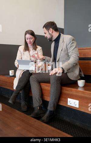 Man and woman sitting together on wooden bench reviewing documents in bright modern office. Document review, teamwork, bright, workspace, discussion. Stock Photo