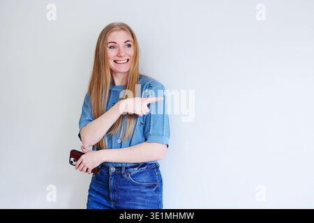 Happy young woman pointing at blank background. Promotion, idea and marketing presentation concept. Stock Photo