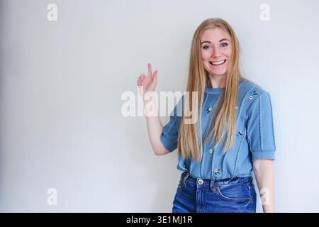 Smiling woman pointing to empty space on wall. Presentation, advertising and copy space concept. Stock Photo