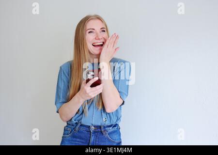 Happy young woman laughing while reading message on smartphone. Mobile communication and modern digital lifestyle concept. Stock Photo