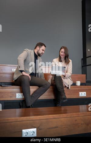 Two business professionals discussing plans and writing notes together on wooden office seating. Plan discussion, note writing, teamwork, business Stock Photo