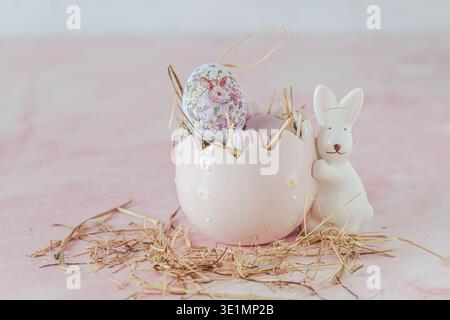 Easter decoration with a porcelain bunny and egg, filled with decorative  pink and purple easter eggs eggs on pink background, copy space Stock Photo
