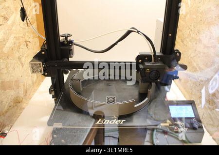 FDM 3D printer producing a plastic object layer by layer on the print bed, demonstrating additive manufacturing technology in a workshop environment. Stock Photo