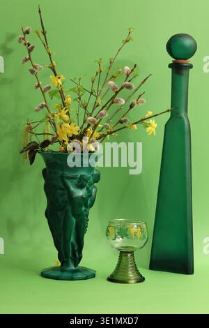 Still life with a green glass vase with plants, bottle and glass. Photo with maximum depth of field on a green background. Stock Photo