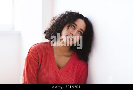 Young Woman Looks Away While Leaning Against a Wall in a Bright Room During the Afternoon Stock Photo