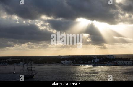 Sun rays breaking through dramatic clouds over the Caribbean Sea near Cozumel, Quintana Roo, Mexico, with light reflecting on the water and coastal ho Stock Photo