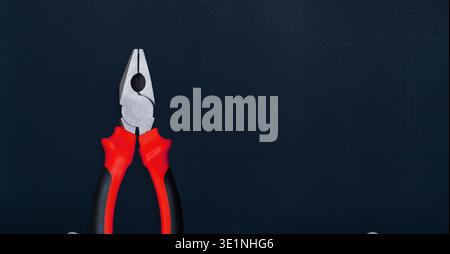 Combination pliers with red and black rubber handles on a dark surface Stock Photo