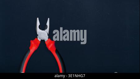 Open combination pliers with red grips over a dark textured copy space Stock Photo