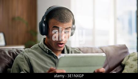 Shock, tablet and man on sofa with headphones for online videos, subscription and watching movies. Home, reaction and person on digital tech for Stock Photo