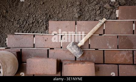 High angle view of masonry work in progress. A rubber mallet rests on freshly laid brown bricks with spacers and wet mortar. Earth tones and a texture Stock Photo