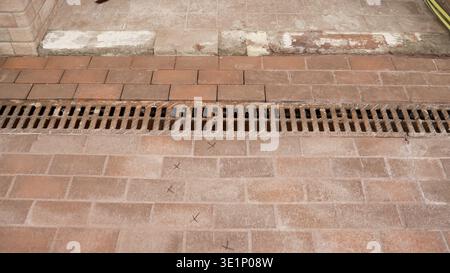 High angle shot of a rustic terracotta brick floor with a metal drainage grate. The worn, old surface in the background contrasts with the new paving. Stock Photo