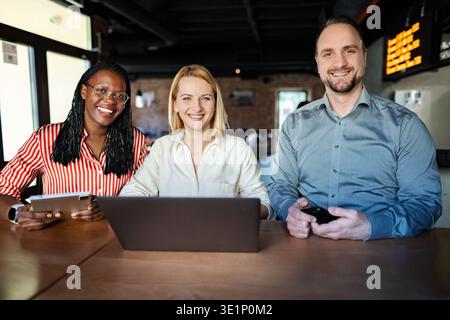 Diverse business team collaborating using technology smiling for camera Stock Photo