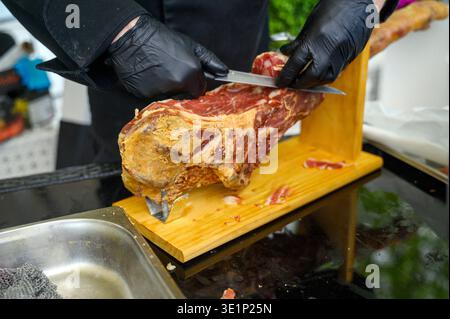 Close up of a seller's hand slicing fresh pieces of dry-cured ham for a guest at a public market. Concept of traditional food trade, hospitality servi Stock Photo