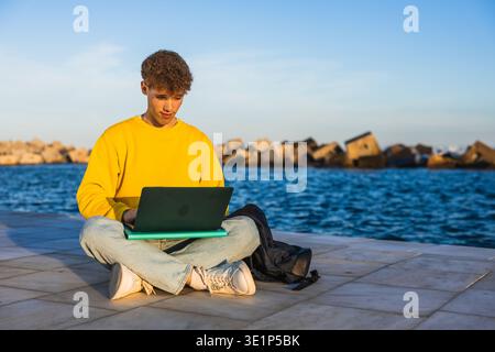 College student working on laptop by the sea at sunset Stock Photo