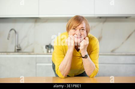 Happy older lady standing in kitchen with warm smile Stock Photo