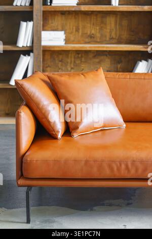 Decorative cushions on brown leather sofa in modern loft office library interior background. Modern business interior with wooden shelves and stylish Stock Photo