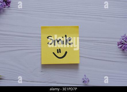 Yellow sticky note with the word smile written on it, symbolizing positivity, happiness, motivation, and daily inspiration. Stock Photo