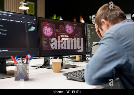 Engineer in startup office doing facepalm, worried after struggling to fix application errors while coding. Distressed IT worker troubled by computer bugs while coding in software development agency Stock Photo