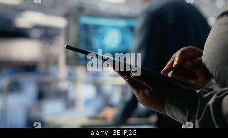 Data center programmers check AI dashboard using tablet, doing systems review. Server hub coworkers test artificial intelligence tools on device to ensure reliable performance, camera B Stock Photo