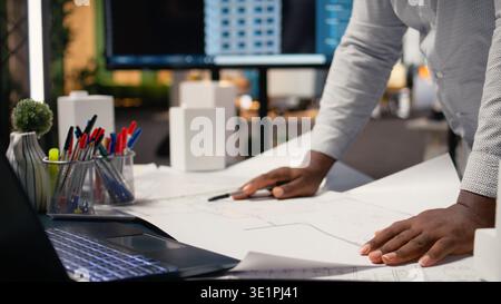 African american contractor examining architectural blueprints plans on table, review zoning regulations for construction project approval. Site preparation master plan and infrastructure. Stock Photo