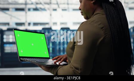 Computer scientist at work using green screen laptop in data center to check hardware for system stability. Manager using mockup notebook to oversee server farm gear, camera B Stock Photo