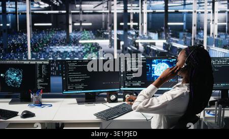 System administrator in data center wearing headset assisting users with artificial intelligence troubleshooting. IT expert in server farm managing support tickets using machine learning, camera A Stock Photo