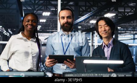 Happy data center coworkers monitoring neural network AI LLM visualization. Jolly workers in high tech facility using devices to oversee servers powering machine learning processes, camera A Stock Photo