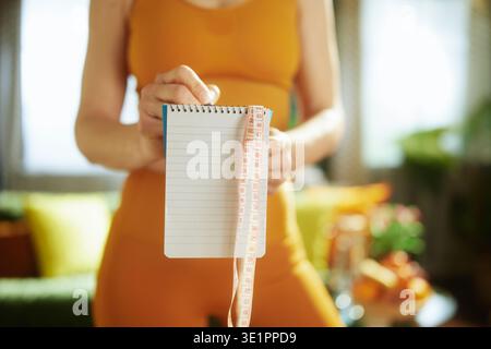 A close-up view of a womans hands holding a blank spiral notebook and a measuring tape, representing the start of a personalized health, nutrition, an Stock Photo