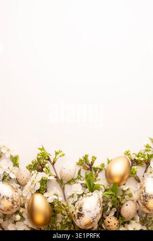 Gold and speckled eggs are placed among white flowers on a plain white background. This scene is set up for the Easter holiday during the spring seaso Stock Photo