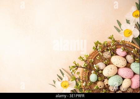 A woven basket holds decorated eggs in various colors. White flowers and green leaves surround the basket. The scene captures the spirit of Easter dur Stock Photo