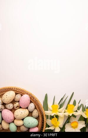A basket filled with assorted eggs in different colors sits next to yellow flowers. This scene shows a spring celebration setting. The background is p Stock Photo