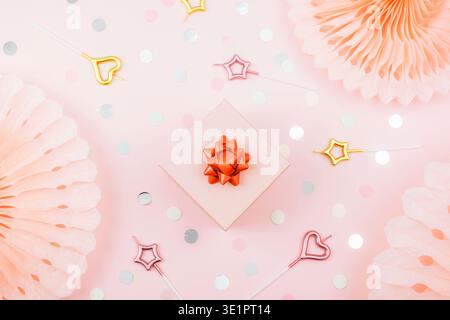 Gift box, candles, colorful confetti and tissue paper fans on pink background. Birthday party concept. Top view, flat lay Stock Photo