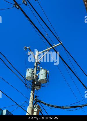 A utility pole stands tall with transformers attached. Many cables stretch out in different directions across a bright blue sky. The scene captures ur Stock Photo