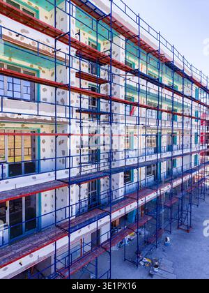 Workers are busy at a construction site where scaffolding supports the outer walls of a multi-story building. Tools and materials are scattered around Stock Photo
