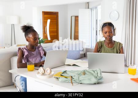 Two African American children responding to homework at table in living room using laptops Stock Photo