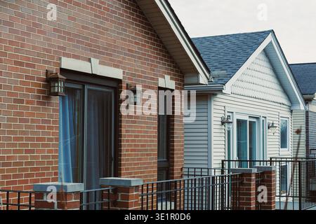 Two different houses with brick and siding facades stand side by side. The buildings are in a neighborhood with clear skies and visible balconies. Stock Photo