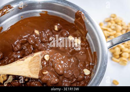 Homemade chocolate peanut clusters being stirred in a metal pot, showcasing a rich, glossy melt and crunchy nuts during the candy-making process. Stock Photo