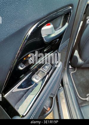 A close-up look at the controls on the door of a car. The view shows window switches, a door handle, and part of the seat. Light is coming in from out Stock Photo