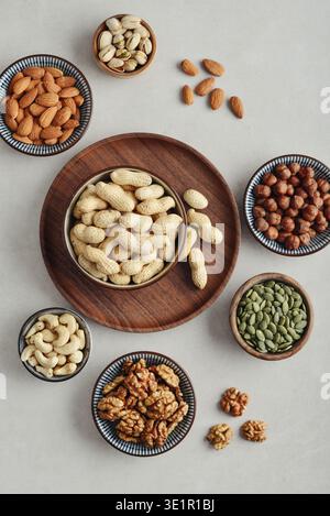 Walnuts, cashews, almonds, hazelnuts, peanuts, pistachios and pumpkin seeds in plates on a light background, top view Stock Photo