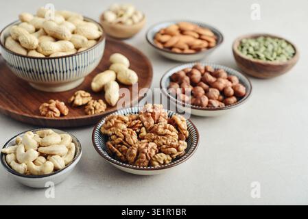 Walnuts, cashews, almonds, hazelnuts, peanuts, pistachios and pumpkin seeds in plates on a light background, closeup Stock Photo