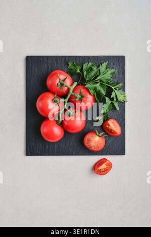 A branch of pink cocktail tomatoes on black square slate plate on a light background, top view Stock Photo