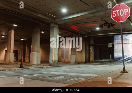A stop sign is visible at the entrance of a parking garage while shadows fall on the ground and columns support the ceiling. Stock Photo