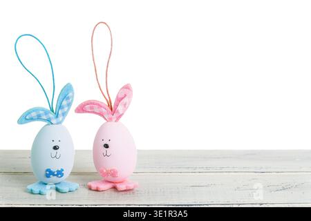 Two decorative Easter eggs with bunny ears, one blue and one pink, placed on a rustic wooden table with a clean white background Stock Photo