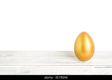 A shiny golden egg placed on a rustic wooden table against a clean white background, highlighting its smooth surface and vibrant color Stock Photo