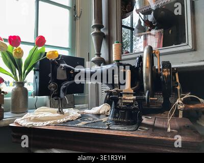 A vintage sewing machine stands on a classic wooden table, forming a single integrated piece typical of older interiors. Fresh tulips nearby Stock Photo