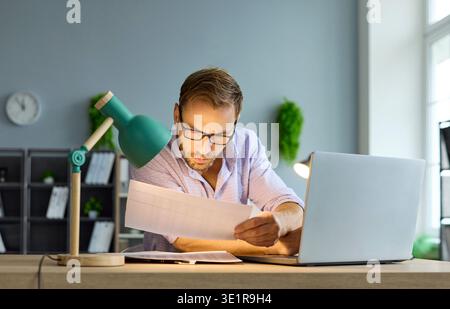 Serious male accountant checking reports and taxes with laptop at office desk Stock Photo
