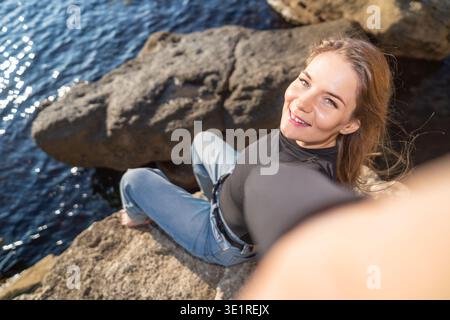 Woman selfie coast smiling young lady taking photo on rocky shore during summer vacation travel Stock Photo