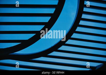 A professional low-angle shot of a modern architectural structure featuring parallel black metal bars and flowing curved steel elements. The geometric Stock Photo