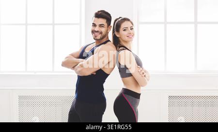 Successful couple standing back to back in studio with big windows Stock Photo